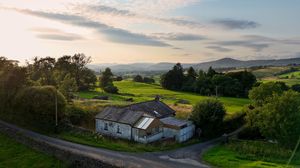 Scenic panorama of rolling hills and rural landscape at sunset with scattered buildings.