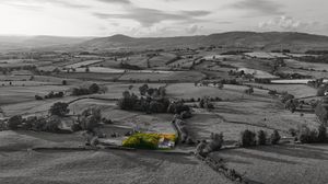 Black and white panoramic landscape of rolling countryside with highlighted building in distance.