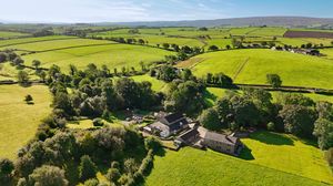 Aerial panorama of lush green farmland with patchwork fields and scattered buildings.