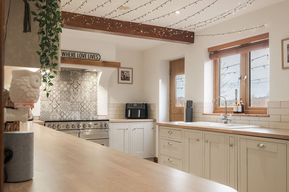 Rustic-modern kitchen with exposed beams, white cabinets, and string lights creating warm ambiance.