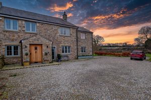 Stone cottage exterior with gravel driveway under dramatic sunset sky.