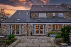 Panoramic view of stone farmhouse exterior during golden sunset with dramatic clouds.
