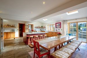 Modern country kitchen with red dining bench and stone flooring featuring an open plan layout and natural lighting.