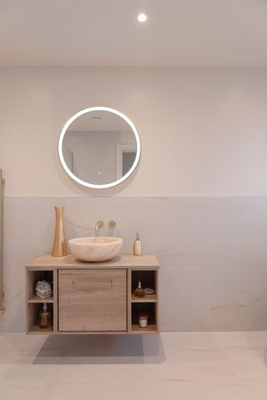 Modern bathroom vanity with circular LED mirror and vessel sink on floating wooden cabinet.