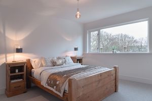 Spacious bedroom with wooden furniture and white bedding in natural daylight.