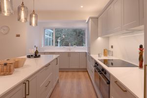 Modern white kitchen with pendant lights, wooden floors, and large window above sink.