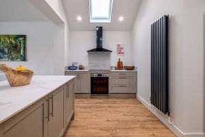 Modern white kitchen with wooden flooring and skylight featuring sleek appliances.