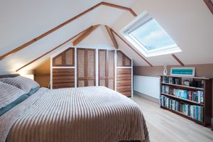 Cozy attic bedroom with striped bedding, wooden panels, and built-in bookshelf under sloped ceiling.