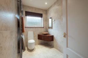 Modern bathroom interior with floating wooden vanity, white toilet and large window offering natural light.