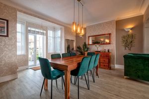 Elegant dining room with teal velvet chairs, wooden table, and pendant lighting.