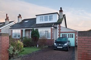 Charming pink bungalow with dormer windows, brick pillars, and attached garage featuring a modern car in the driveway.