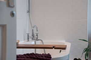 Close-up of a modern bathroom faucet and wooden bath caddy against white subway tile.