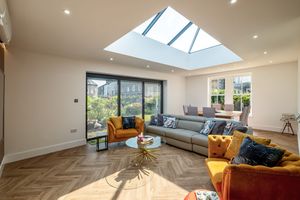 Modern living room with skylight, grey sofa, mustard accent chairs, and sliding glass doors.