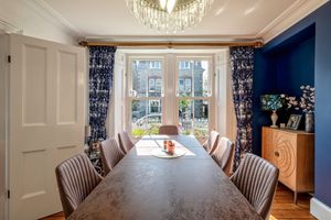 Formal dining room with blue curtains, upholstered chairs, and large windows overlooking garden.