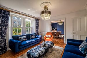 Luxurious living room with blue velvet sofas, patterned ottoman, and crystal chandelier.