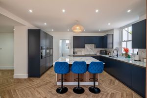 Contemporary kitchen with navy cabinets, herringbone flooring, and blue bar stools at the island.