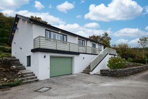 Modern white hillside house with green garage door, exterior stairs, and stone wall features.