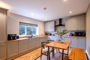 Spacious grey kitchen with wooden dining table, modern appliances and abundant natural lighting.