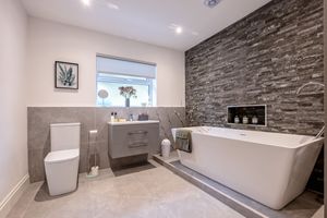 Contemporary bathroom featuring freestanding tub, stone accent wall, and modern fixtures in neutral tones.