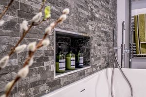 Bathroom detail showing stone wall niche with glass bottles and decorative pussy willow branches.