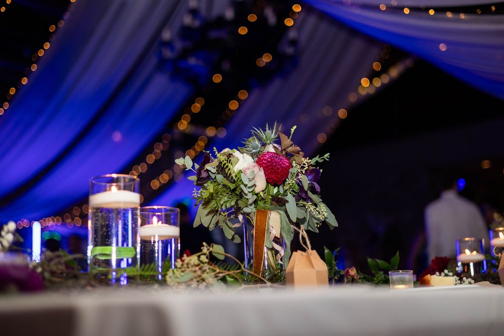 A wedding reception at Knights at Castle Farms decorated with blue uplighting and elegant floral centerpieces on dining tables.