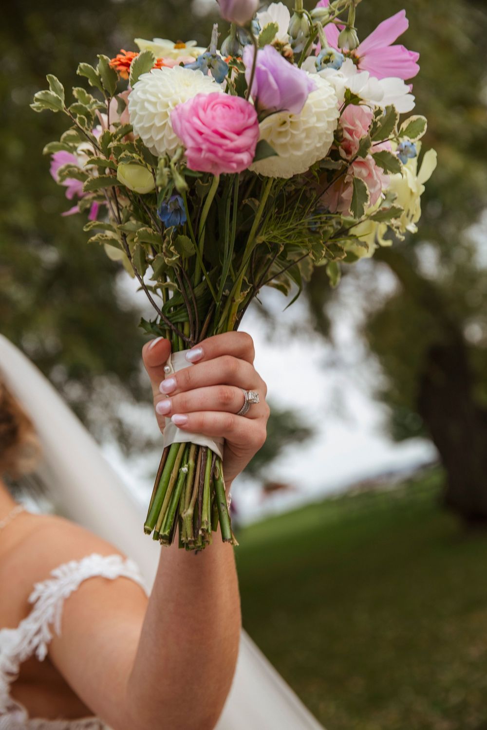 A beautiful wedding bouquet with pink and white flowers held against a blurred outdoor background.