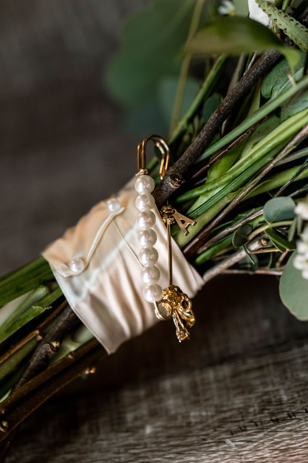 Pearl and gold bridal jewelry details arranged with greenery on rustic wooden surface in elegant wedding styling.