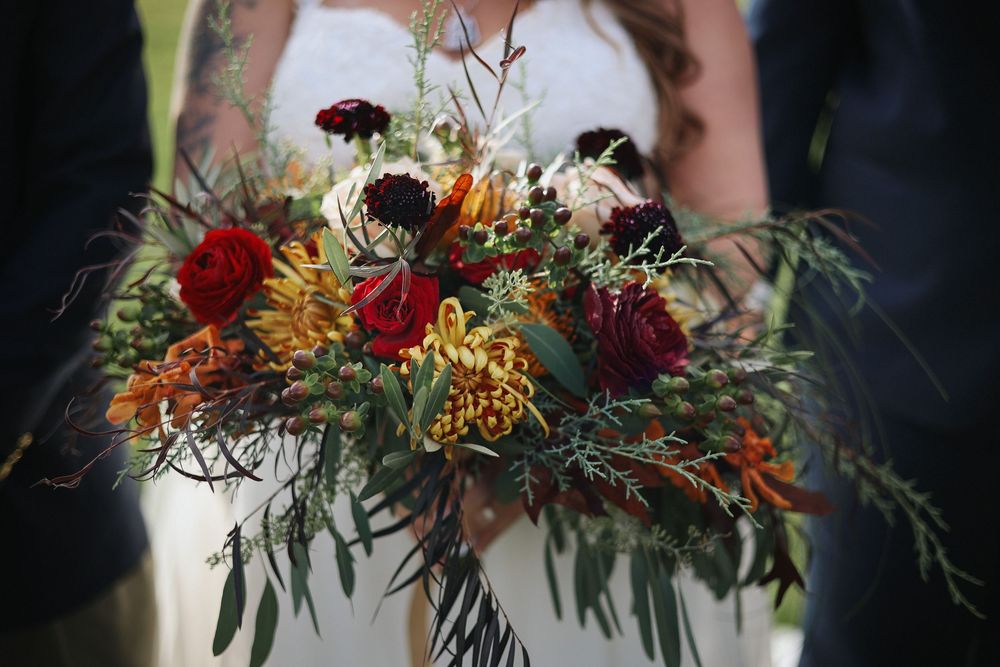 Wedding bouquet featuring deep red roses, orange lilies, and autumn greenery against a dark background on Mackinac Island.