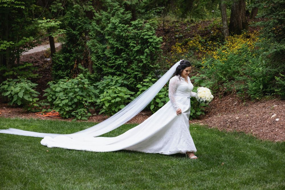 A flowing white wedding dress with a dramatic long veil catches the breeze in a lush garden setting.