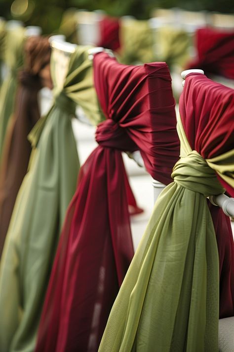 Elegant wedding chairs decorated with draped burgundy and sage green fabric sashes tied in knots.