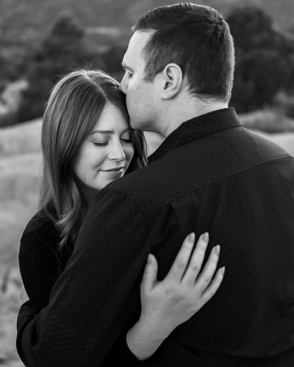 A romantic black and white photo showing a couple in an intimate embrace outdoors.
