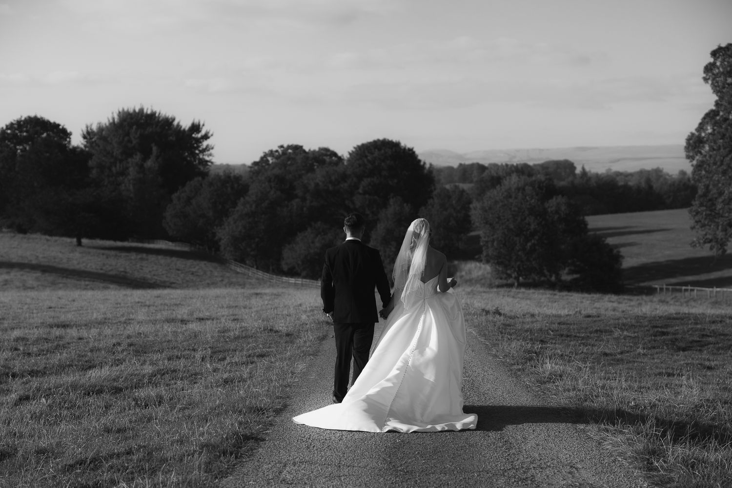 A black and white wedding photo series showing a couple walking through scenic outdoor landscapes and fields.