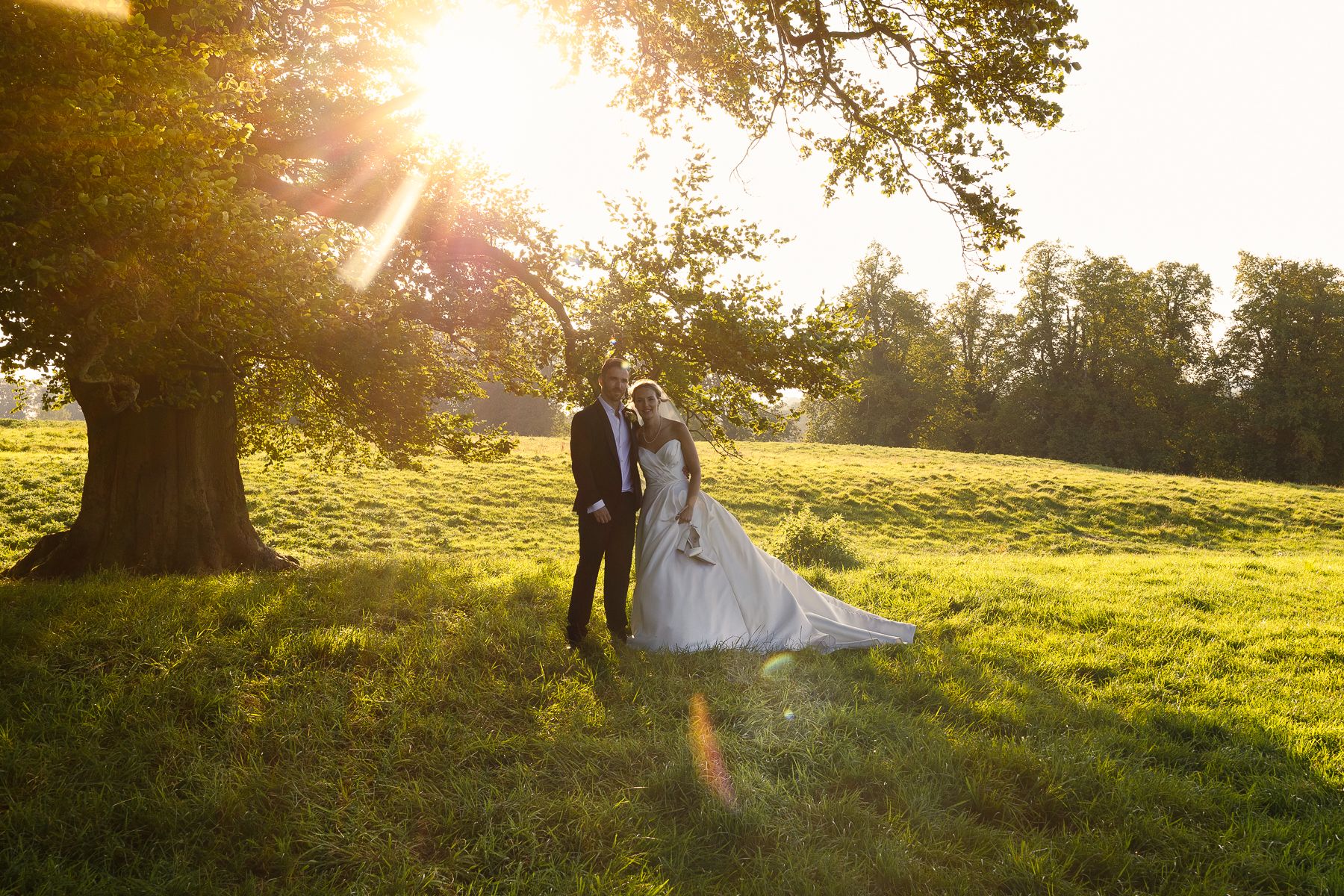 Couple in wedding attire poses in golden sunlit meadow during sunset photography session.