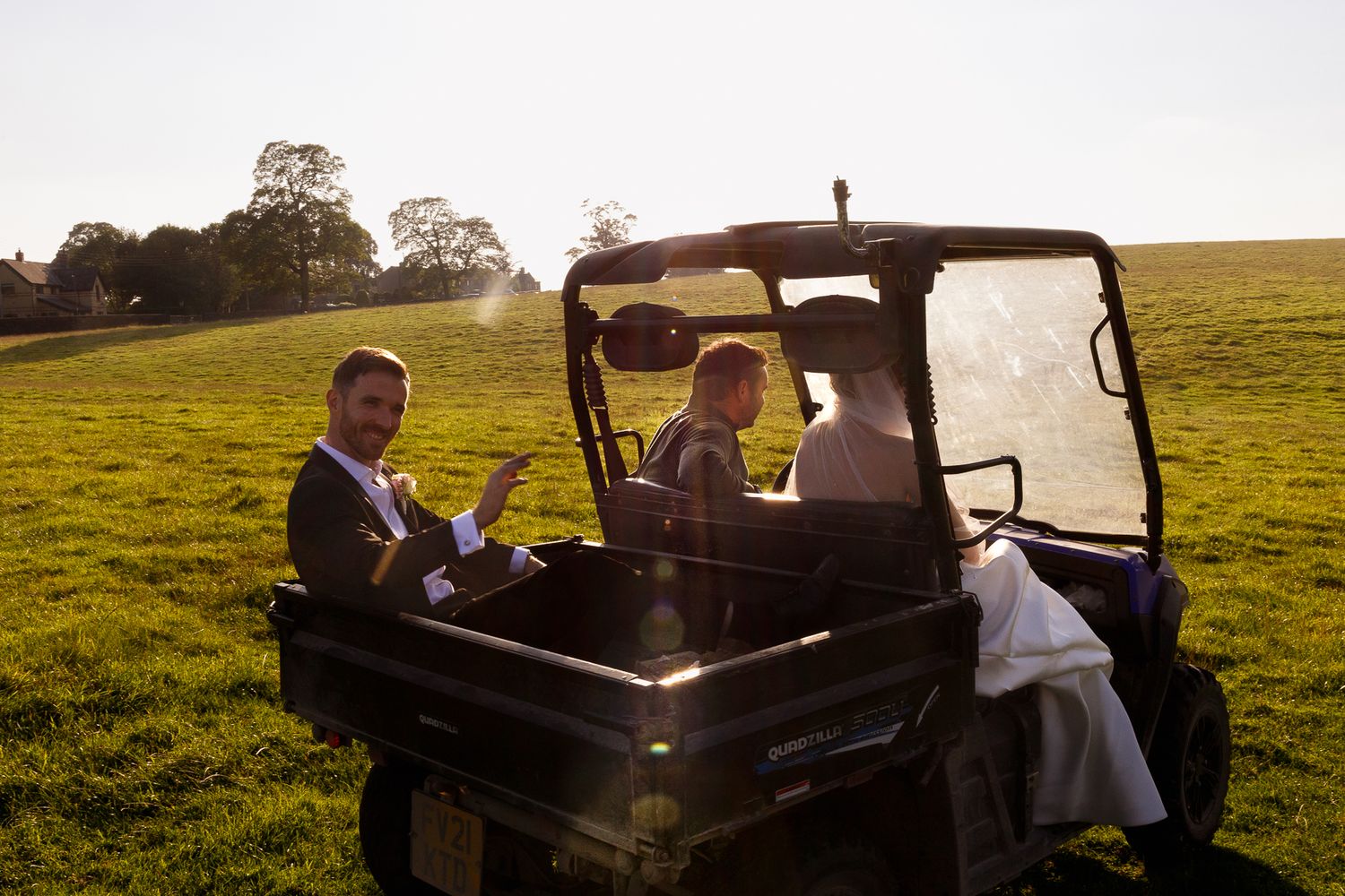 A couple rides in a vintage car through a golden sunlit field during a countryside photo session.