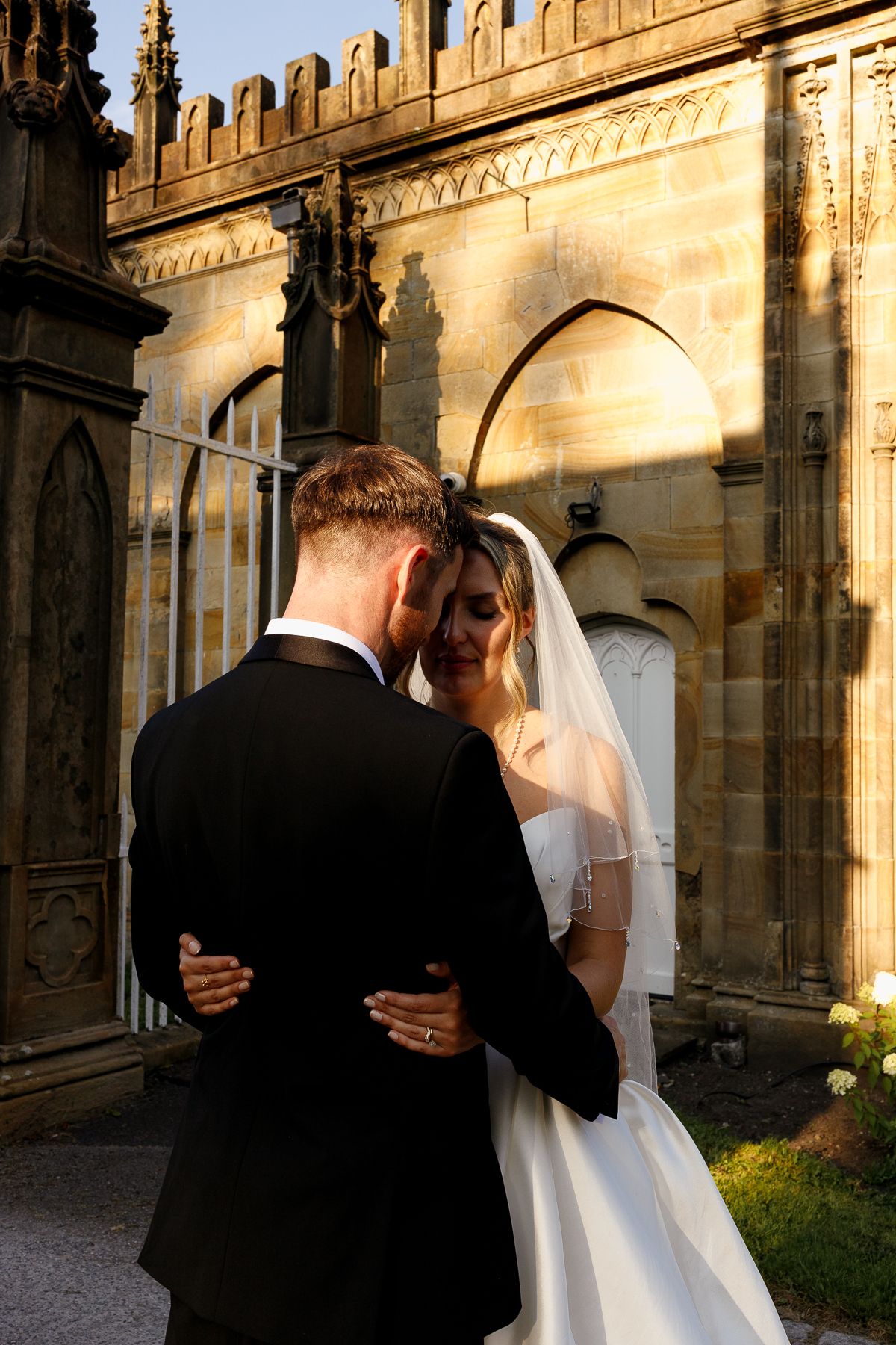 Romantic wedding couple embraces in a series of intimate moments against a historic stone building at sunset.