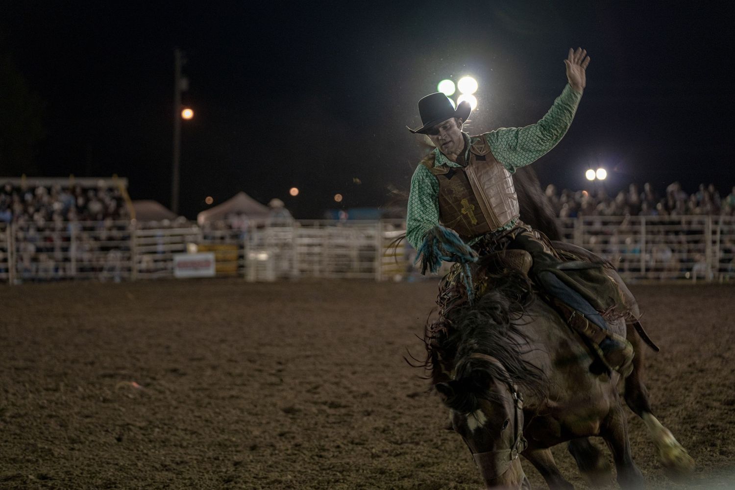 A rodeo rider attempts to stay mounted on a bucking horse during a nighttime competition at an arena.
