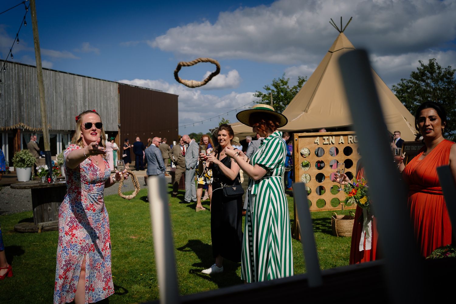 People gather outdoors near a teepee structure during a historical reenactment event on a sunny summer day.