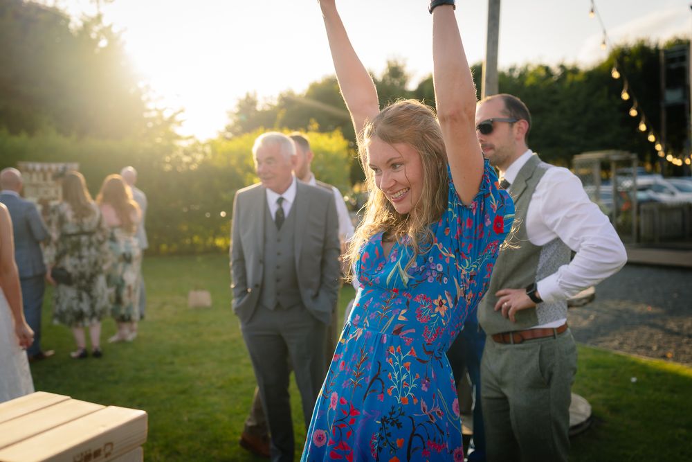 Wedding guests play giant Jenga at an outdoor sunset reception celebration.