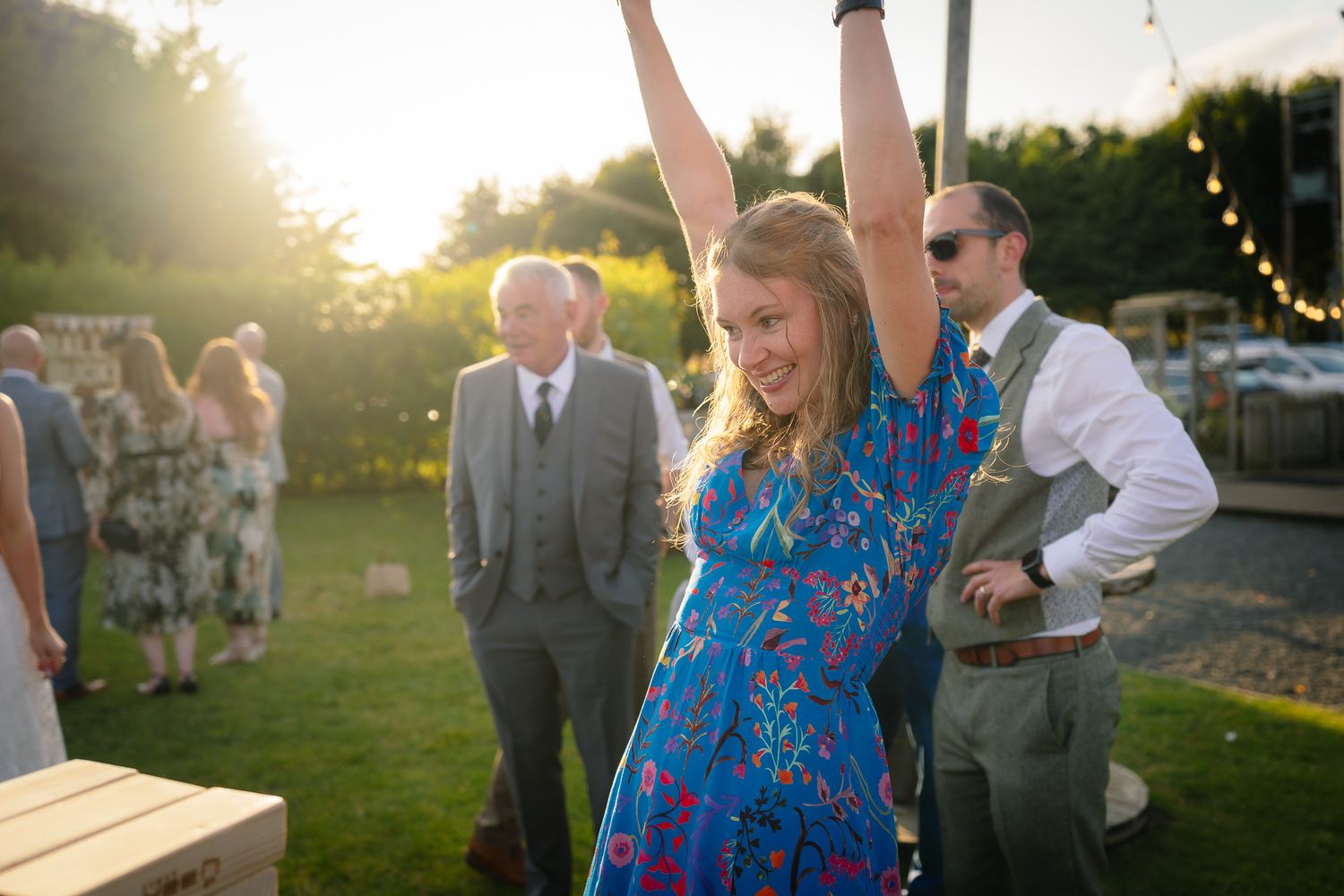 Wedding guests play giant Jenga at an outdoor sunset reception celebration.