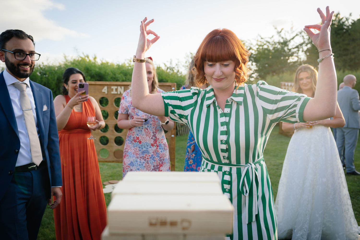 Wedding guests dance joyfully outdoors at a celebration with trees and natural scenery in the background.