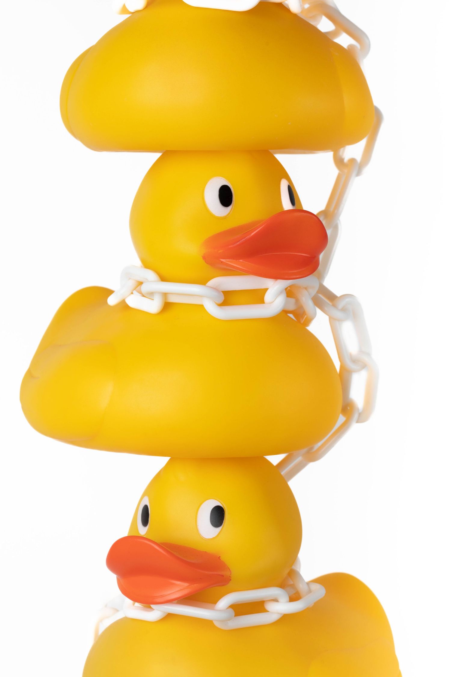 Three stacked yellow rubber ducks connected by white plastic chains against a white background.