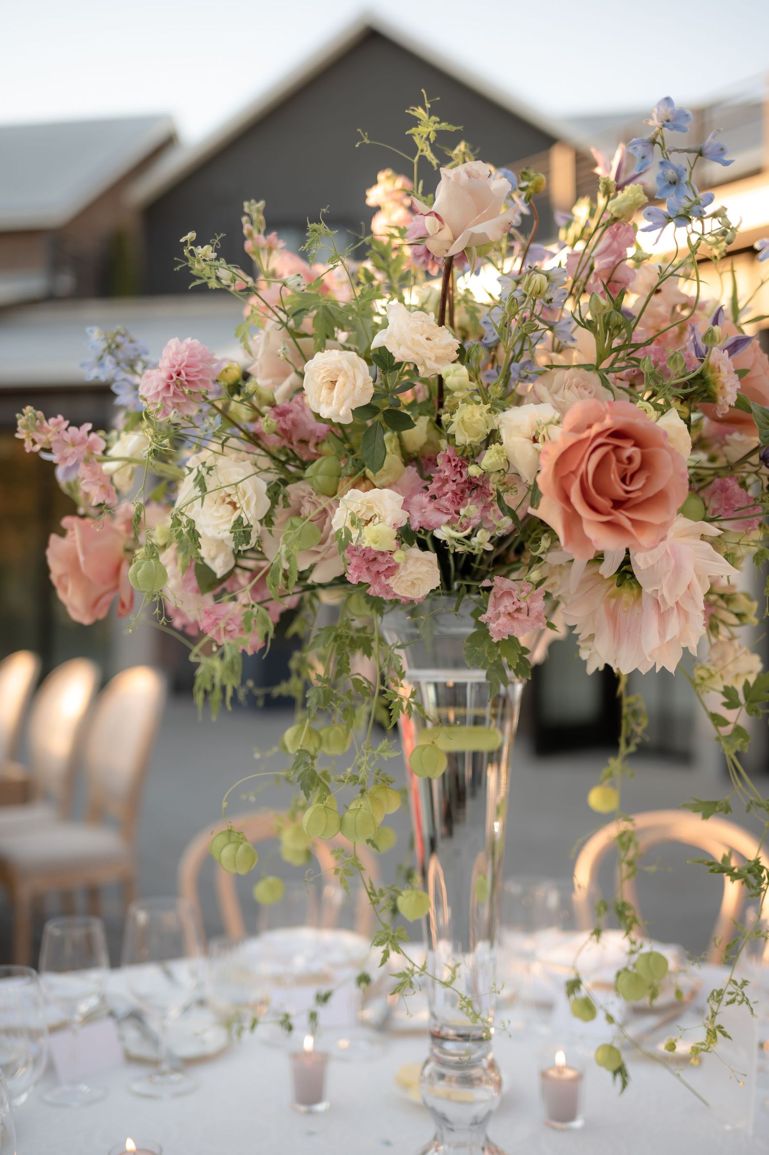 Elegant floral centerpieces featuring pink roses, white blooms and greenery in tall glass vases on white tablecloths.