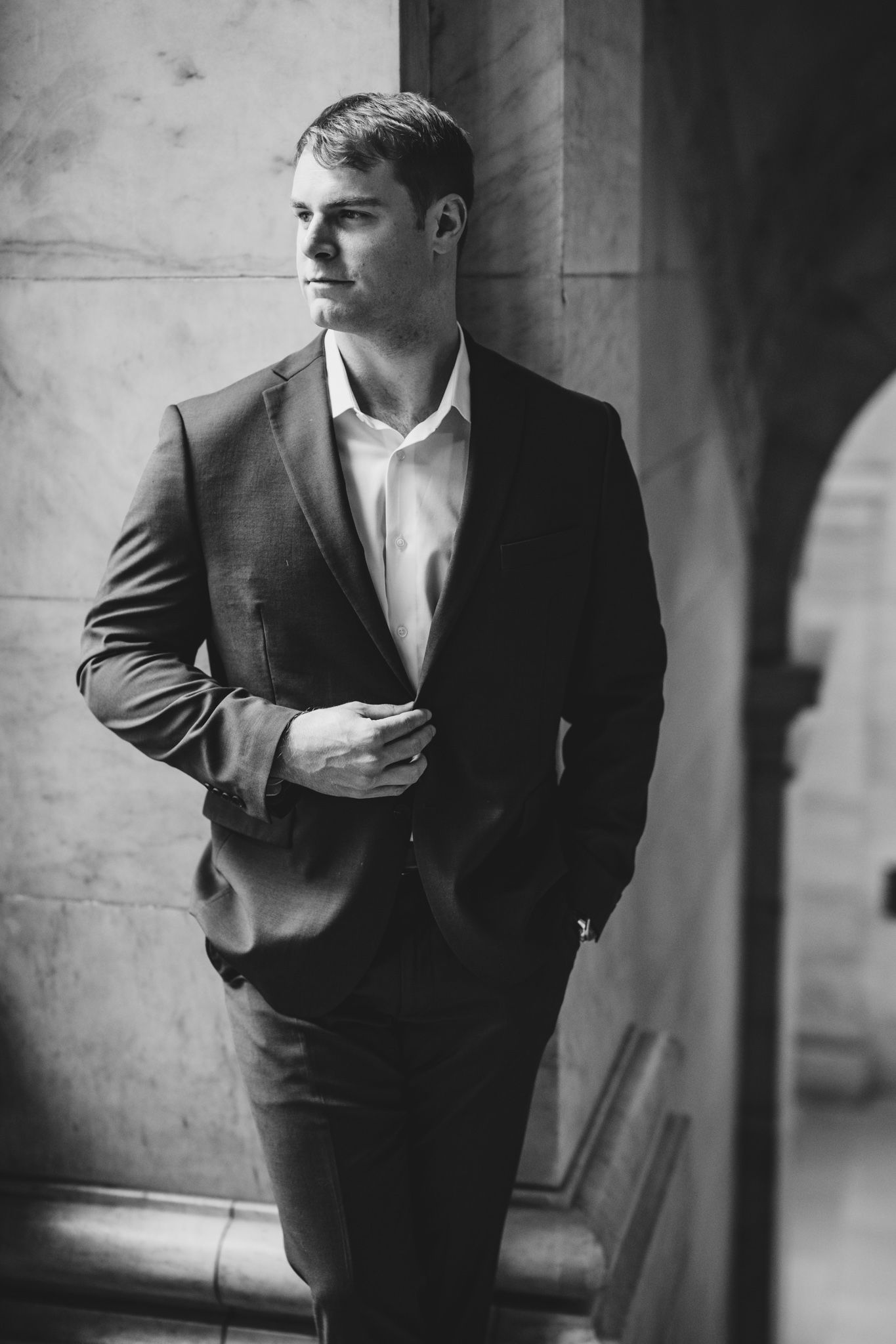 Dramatic black and white portrait in formal attire against stone architecture.