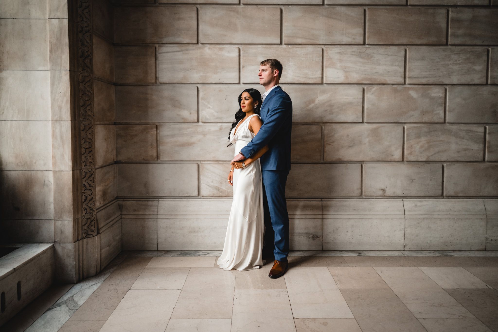 A couple shares an intimate moment against a stone wall in a romantic engagement photoshoot.