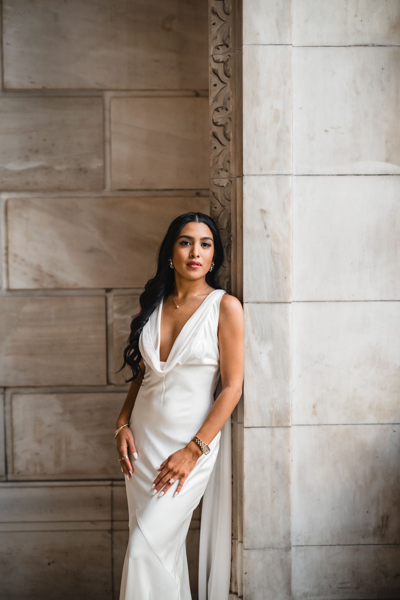 Person in a white dress poses elegantly against a stone wall background.