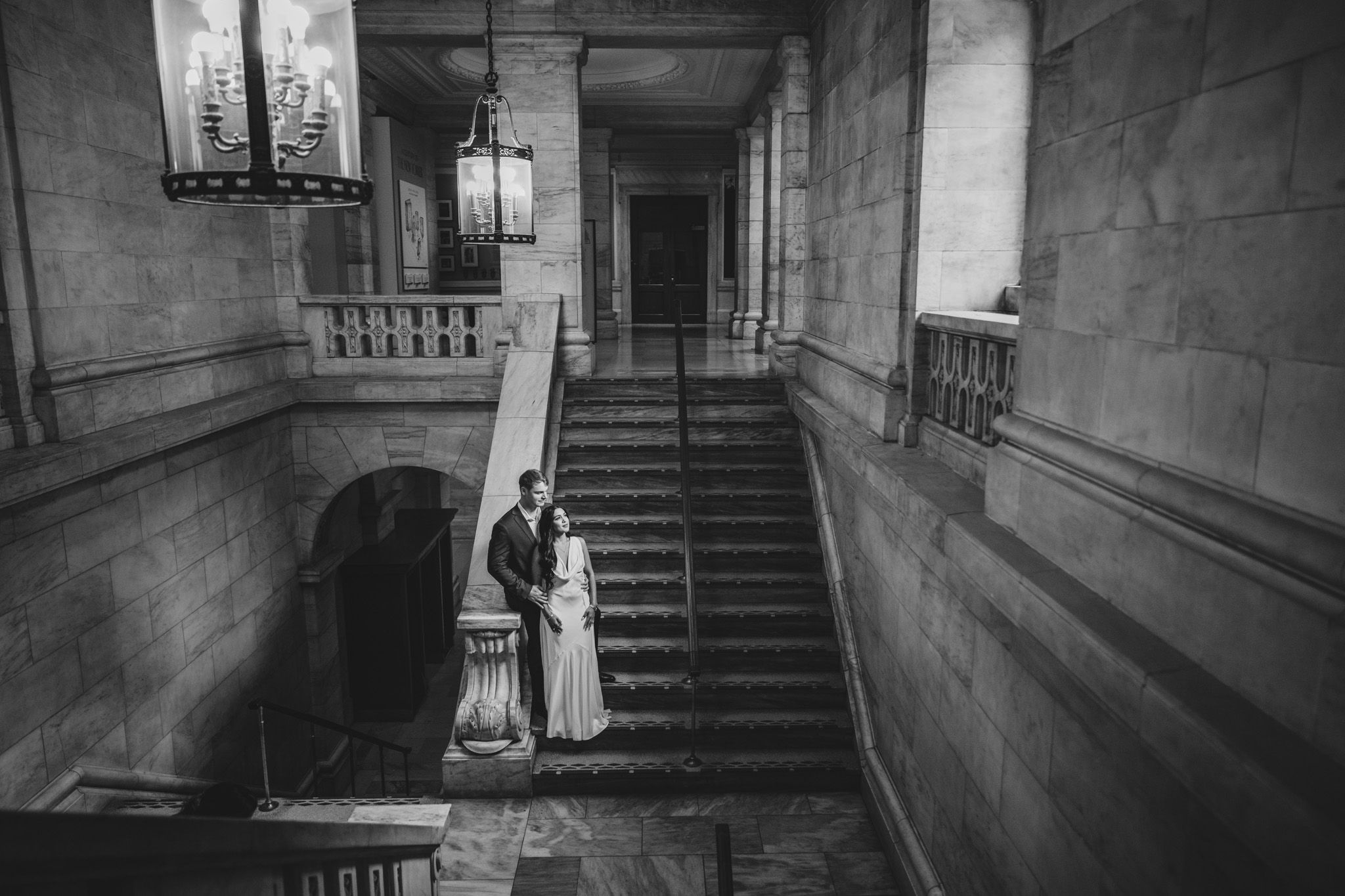 Black and white photo of couple on elegant stone staircase in historic building.