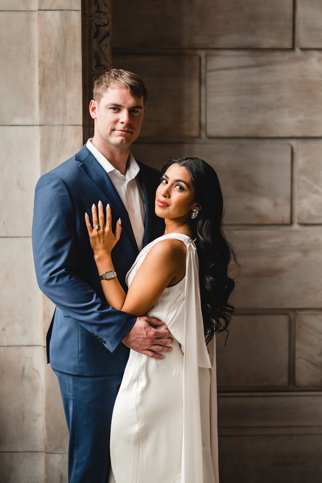 Couple shares romantic poses against stone wall during engagement photo session.