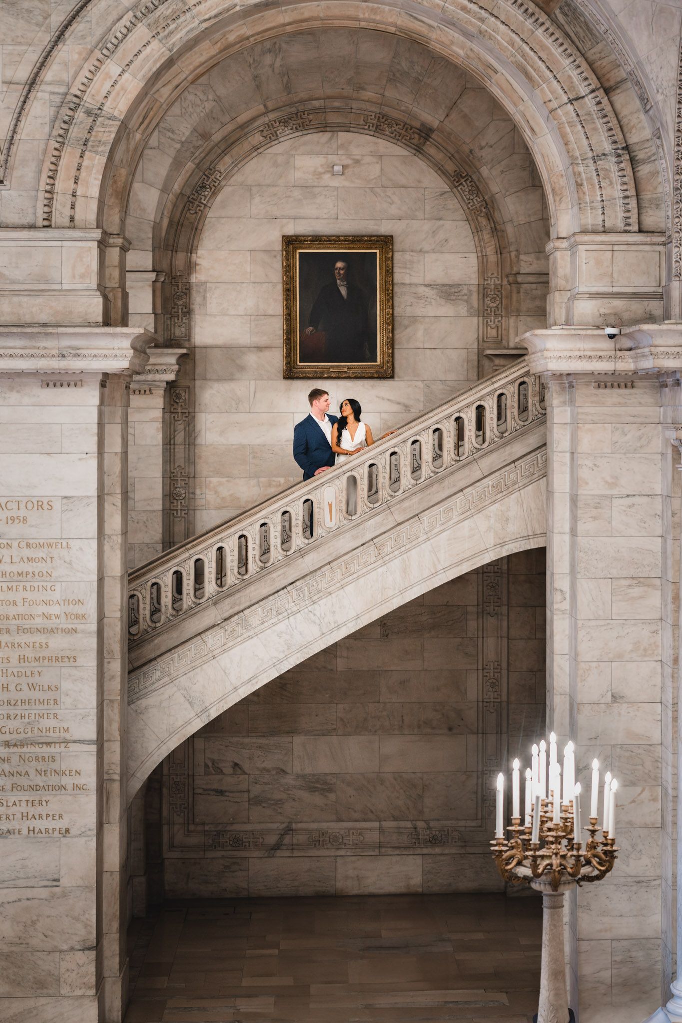 Couple shares an intimate moment in a grand stone archway with ornate architectural details and candlelight.