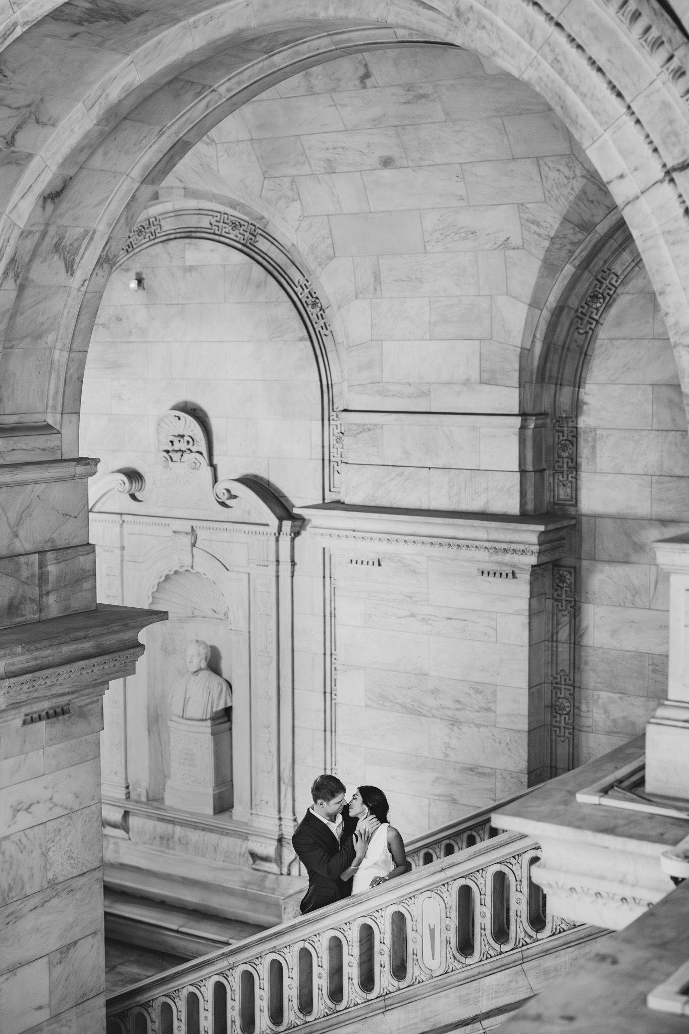 Couple embraces in a majestic stone corridor with classical architectural features.