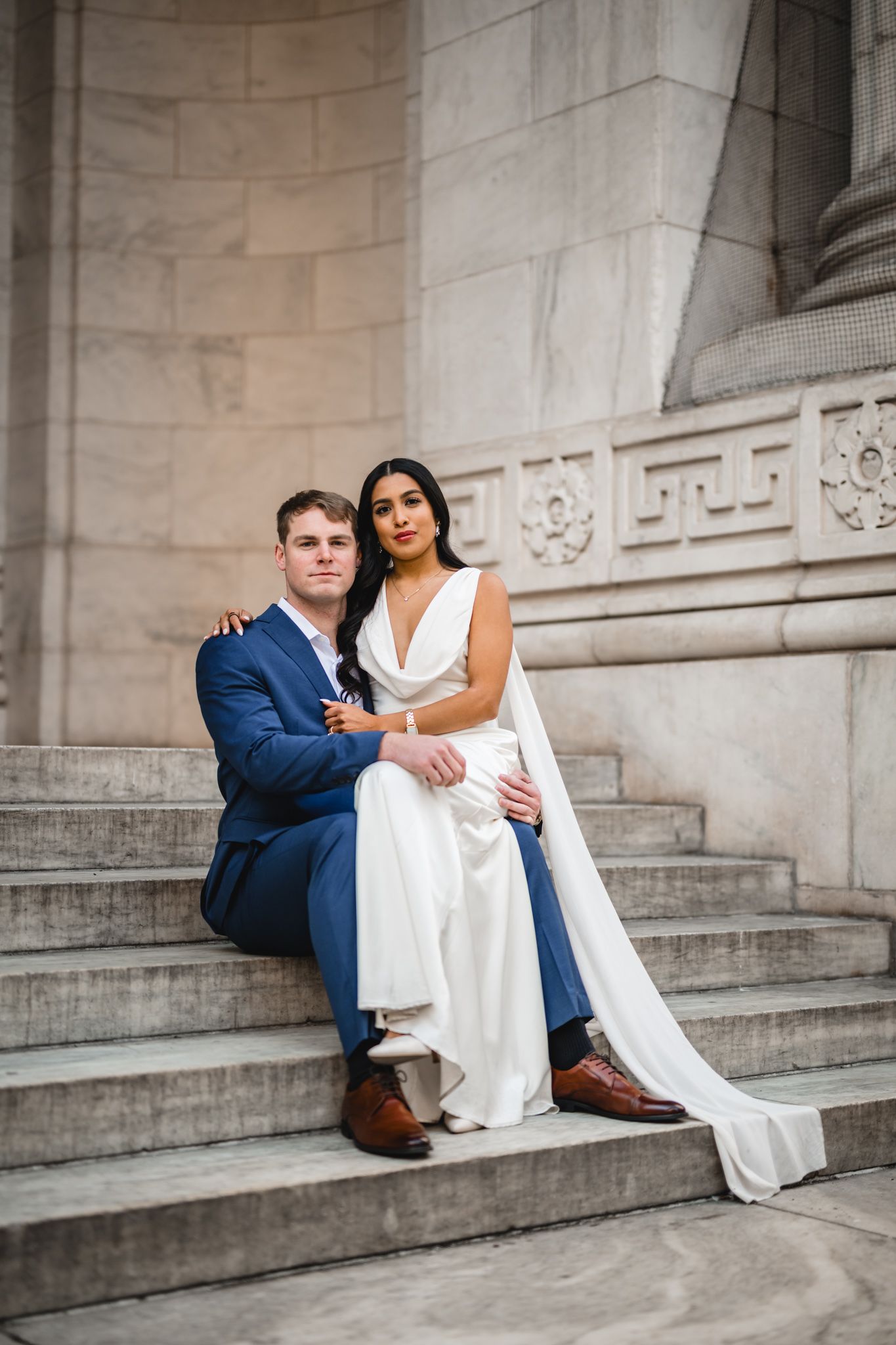 Elegant couple posed on grand marble staircase in formal attire.